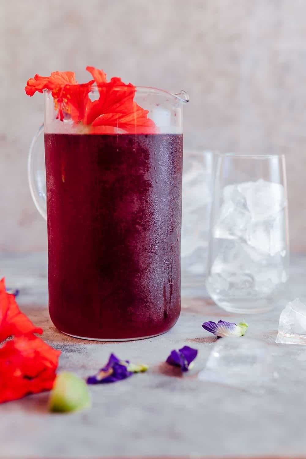 Aprenda a fazer chá de hibisco, que tem alguns benefícios surpreendentes. Faça isso com flores frescas ou secas e escolha tê-lo como uma xícara quente de chá ou como chá gelado de hibisco, porque de qualquer forma é delicioso e muito bom para você! #hibiscus #healthfood #drink #icedtea #summer #recipe Chá de hibisco gelado servido em uma jarra grande com flores frescas de hibuscus